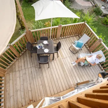 Sunlit wooden deck with a dining table, parasol, and a person lounging.