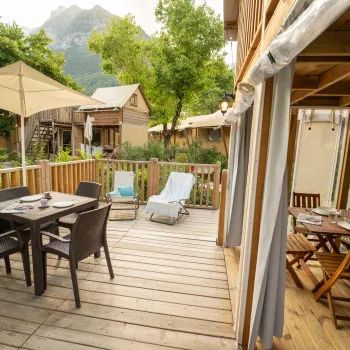 Wooden patio with tables, chairs, and umbrellas surrounded by greenery and mountains.