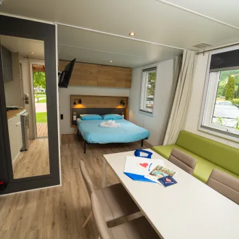 Modern hotel room with a double bed, table, and sofa. Bright natural light.