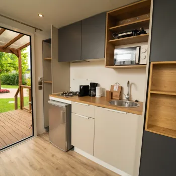 Compact kitchen with gray cabinets, appliances, and an open door to a patio with greenery.