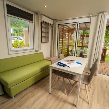 Cozy room with green sofa, table, and large windows opening to a garden view.