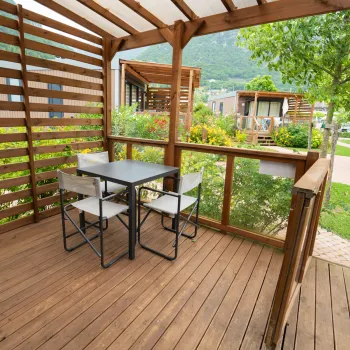 Deck with table and chairs, surrounded by greenery and trees.