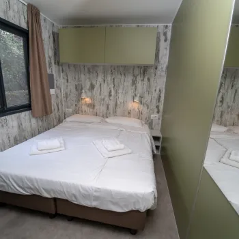 Cozy bedroom with a double bed, wall lamps, mirrored closet, and window with brown curtains.