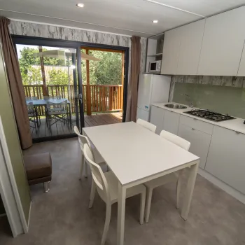 Modern kitchen with white table and chairs, opening to a balcony with greenery.
