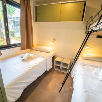 Two beds, one bunk, in a cozy room with a window and two lamps.