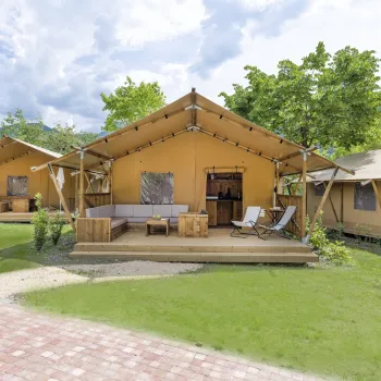 Luxury camping tents on lush green lawn with trees and cloudy sky.