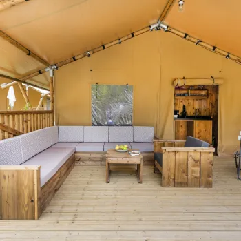 Outdoor patio with wooden seating, small table, and a canvas tent roof.