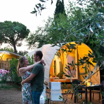Couple embraces in a garden near a glowing tent at dusk.