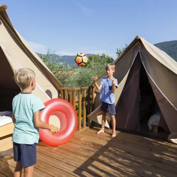 Two children playing on a wooden deck between two tents.