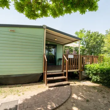 Mobil home with wooden deck, surrounded by trees.
