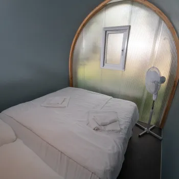 Cozy bedroom with neatly made beds, window and a fan.