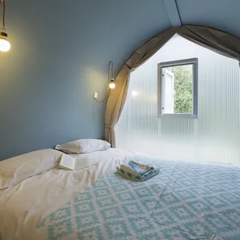 Cozy bedroom with soft lighting, blue walls, and a large window.