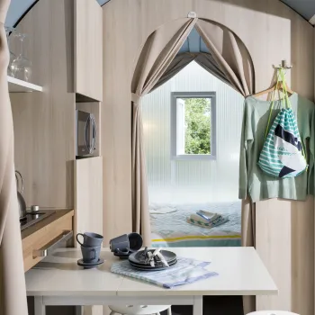 Cozy cabin interior with dining table, kitchenette, and open curtains to a small bedroom.
