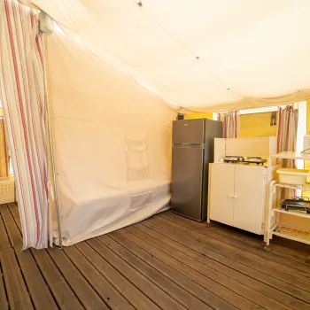 Glamptent kitchen interior with wooden floor, curtains, fridge, shelves.
