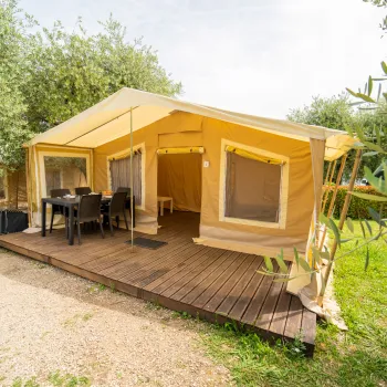Glamptent on wooden deck, surrounded by greenery.