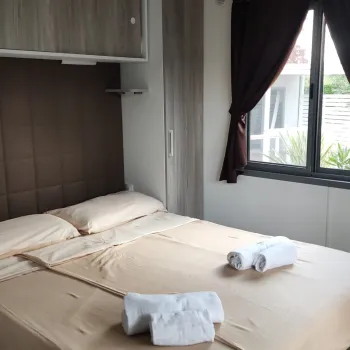 Cozy bedroom with neatly made bed, and large window with dark curtains.