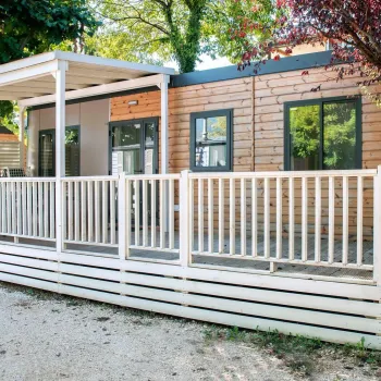 Wooden cabin with a white railing porch under trees.