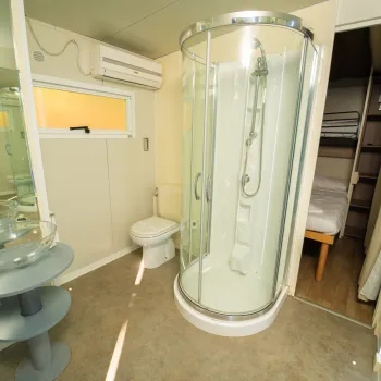 Modern bathroom with shower, sink, and toilet, next to a bedroom.