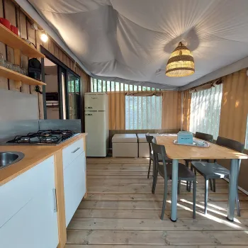 Cozy cabin interior with kitchenette and dining table, wood flooring, soft lighting.