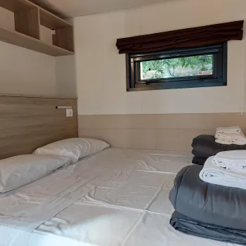 Cozy bedroom with a made bed, folded towels, and sunlight through a small window.