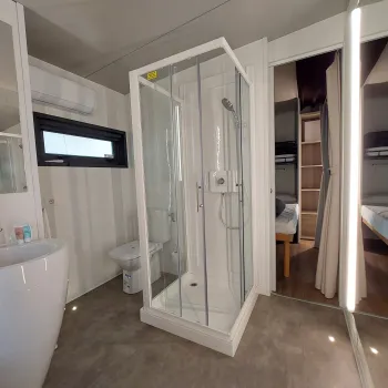 Compact modern bathroom with glass shower and adjacent bedroom.