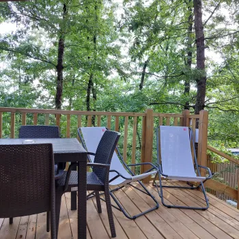 Wooden deck with chairs and table, surrounded by lush green trees.