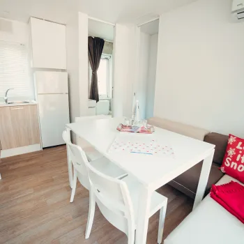 Modern kitchen with white table, chairs, and cozy red-accented sofa.