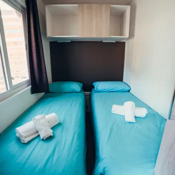 Twin beds with blue sheets and folded towels in a bright room.