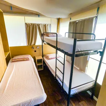 Three beds in a small wooden room, including bunk beds and a single bed.