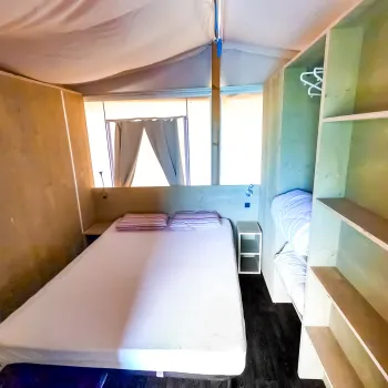 Tent interior with bed, wooden shelves, and curtains.