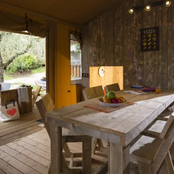 Wooden dining table with chairs in a cozy room, open door to a porch with a bench.