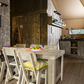 Rustic wooden dining room with table, chairs, and cozy kitchen in background.