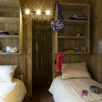 Cozy wooden room with two beds, shelves, and hanging bags.