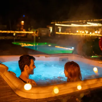 Two people relaxing in a hot tub at night, surrounded by warm lights.