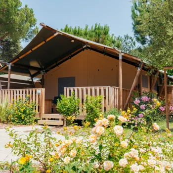 Tent cabin with wooden deck in a garden, surrounded by blooming flowers and trees.