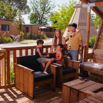 Family relaxing on a wooden porch with cabins in the background.