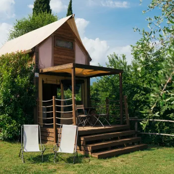 Rustic wooden cabin with a sloped roof, surrounded by greenery. Two chairs in front.