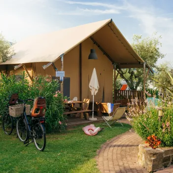 Cozy canvas tent surrounded by lush greenery and a bicycle parked nearby.