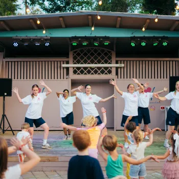Children dance along with performers on an outdoor stage.