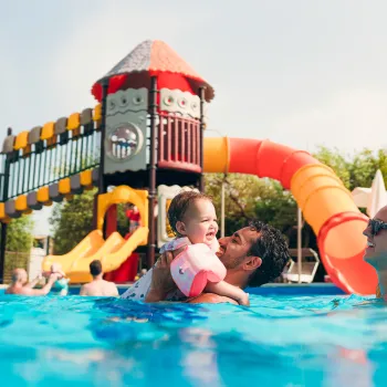 Family enjoying a sunny day at a pool with colorful slides in the background.