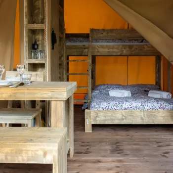 Rustic wooden cabin interior with beds and dining table. Bright orange walls.