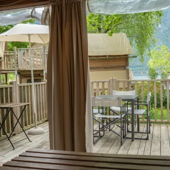 Cozy patio with tables, chairs, and umbrella, overlooking lush greenery and wooden cabins.