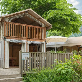 Two-story wooden cabin with a balcony, surrounded by greenery.