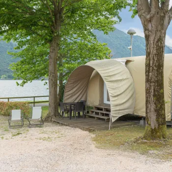 Cozy cabin tent by a lake, with trees and mountains in the background.