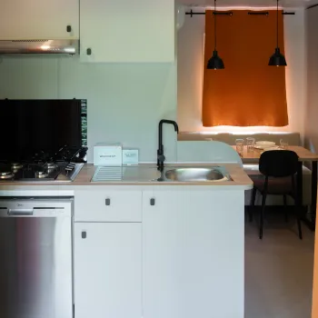 Compact kitchen with white cabinets and orange curtains, next to a cozy dining area.