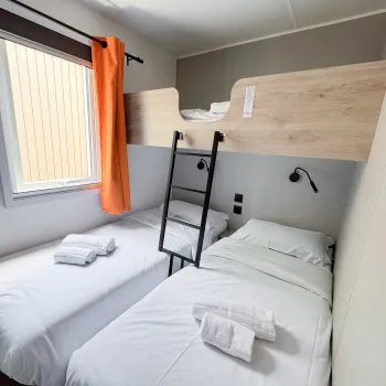 Compact room with two beds, one bunked, white bedding, and an orange curtain.