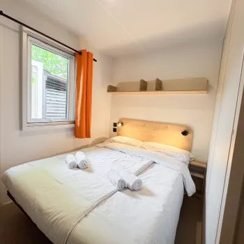 Compact bedroom with a double bed, window, and orange curtains.