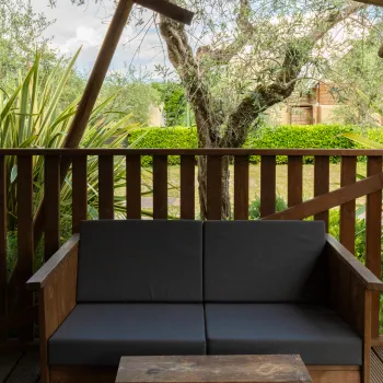Wooden deck with a dark gray sofa, lush greenery in the background.