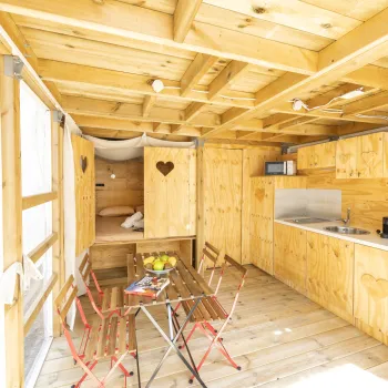Wooden cabin interior with table, chairs, and kitchenette. Bright and cozy atmosphere.