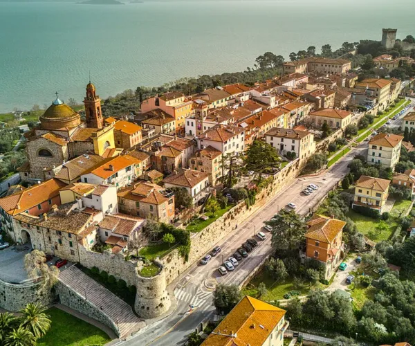Historic coastal town with terracotta rooftops, surrounded by lush greenery and sea.